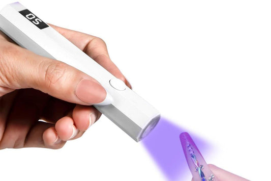 Handheld UV nail lamp applying purple light to manicure nails