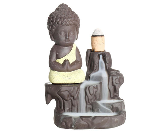 Ceramic Buddha incense backflow burner with yellow robe; incense cone sits atop holder.
