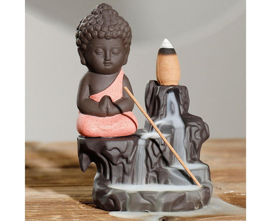 Ceramic Buddha incense backflow burner with pink robe; backflow smoke pool at base.