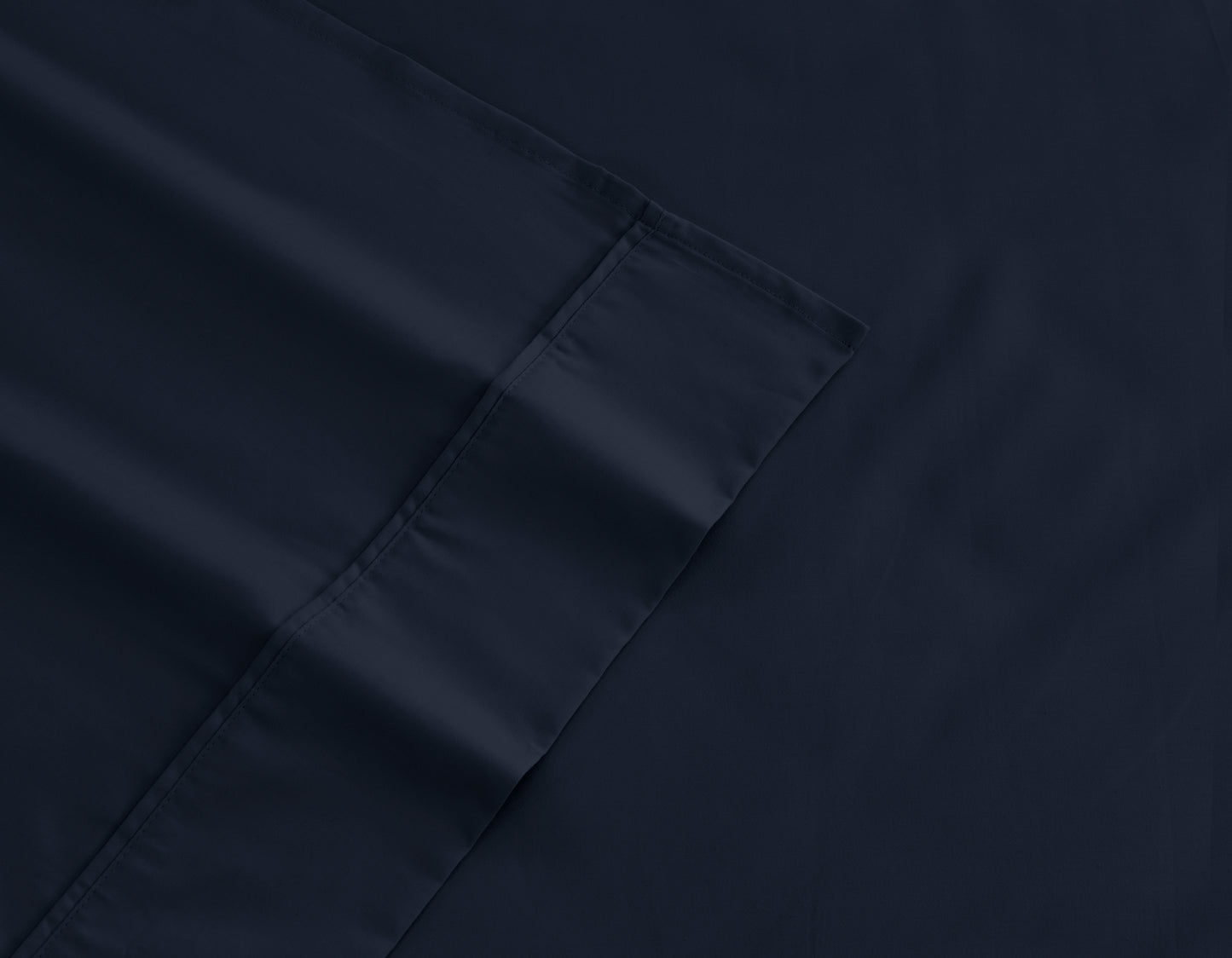 Dark navy cotton-rich sheet fabric close-up with stitched edge and corner hem