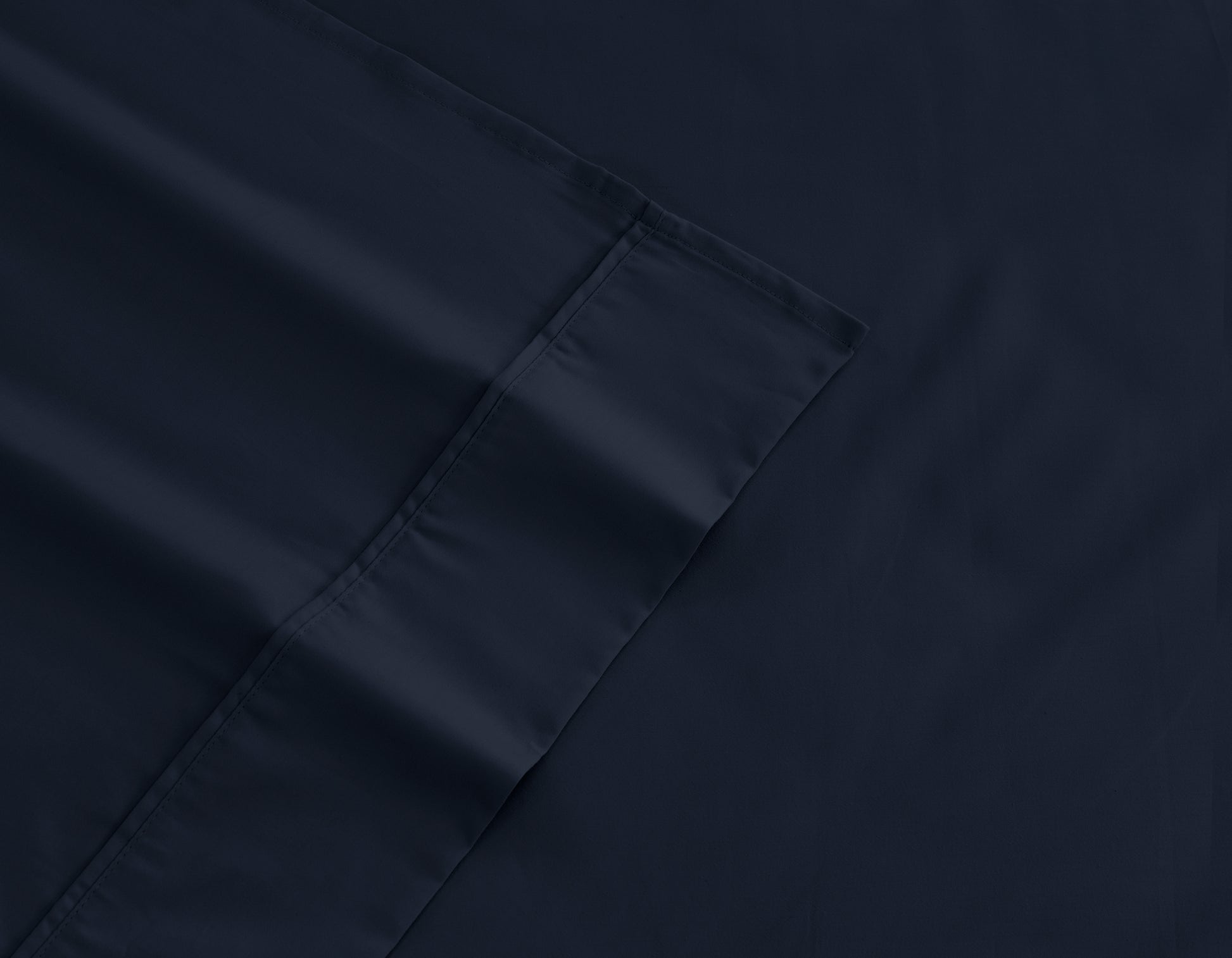 Dark navy cotton-rich sheet fabric close-up with stitched edge and corner hem