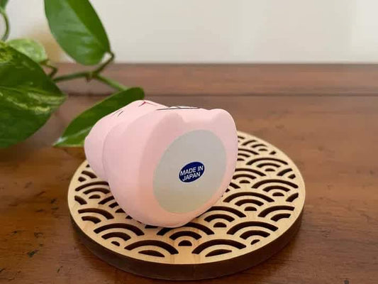 Pink Maneki Neko figurine on patterned circular base, side view