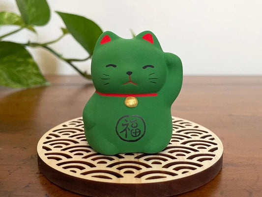 Green maneki-neko cat ornament with gold bell on patterned circular base