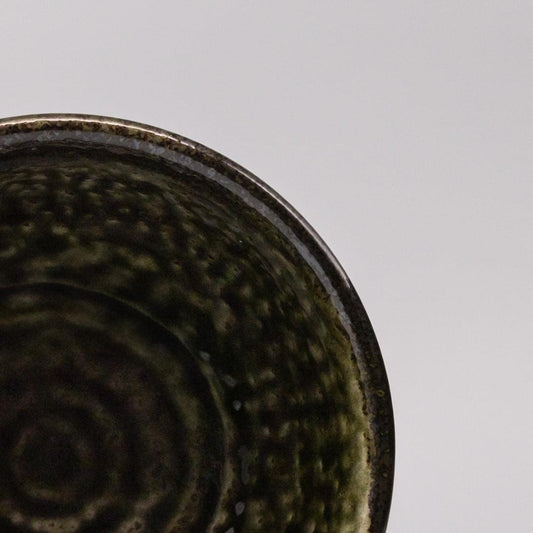 Ceramic bowl interior close-up with dark moss green glaze and swirling pattern