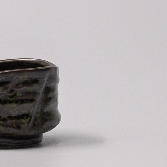 Textured dark ceramic sake cup with moss-black glaze, side view