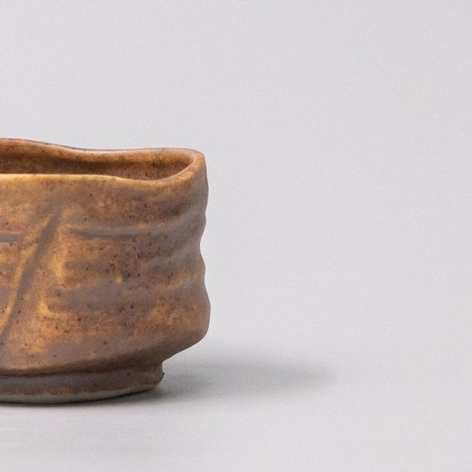 Ceramic sake cup with ochre glazed finish, rounded rim and scalloped texture