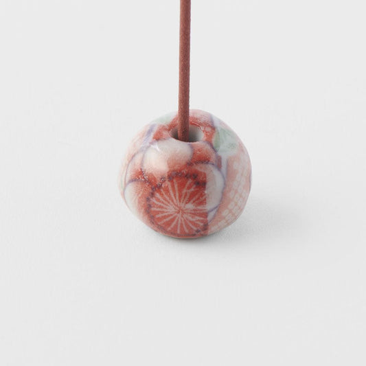 Incense stick inserted in red and white round chiyogami incense holder