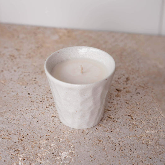 White ceramic candle cup with small flame and visible wick