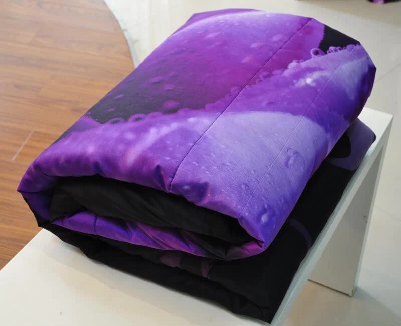 Comforter set folded on table: black layers topped with purple rose floral bedding