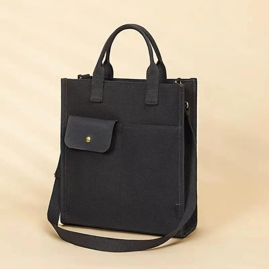 Black canvas tote bag with top handles, front flap pocket, and crossbody strap