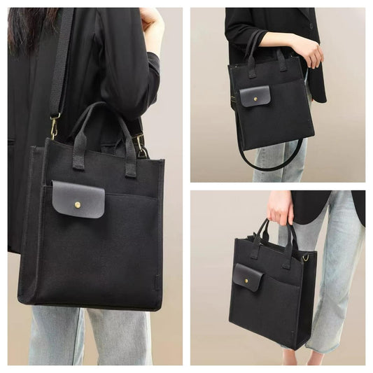 Black canvas tote bag worn over shoulder, with front flap pocket and top handles