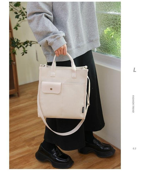 White canvas tote bag with front pocket, top handles, and adjustable crossbody strap