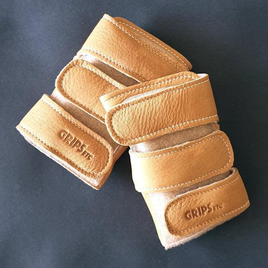 Tan leather wrist savers with stitched bands and Velcro logo tabs, pair