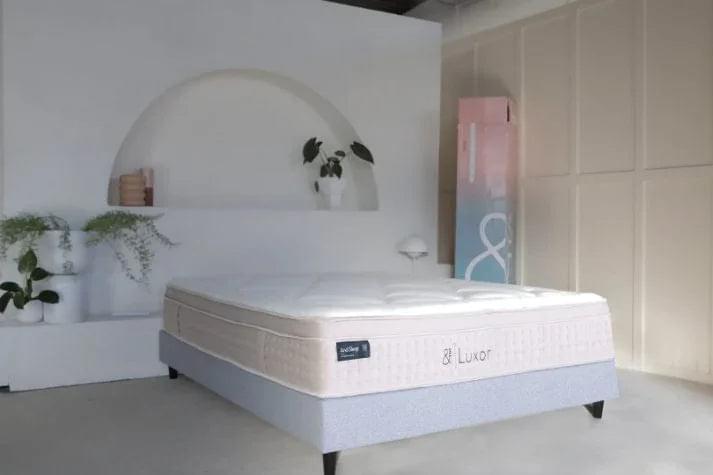 White quilted Luxor mattress on dark base, side & Luxor logo visible
