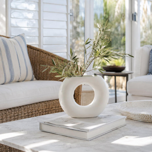 White ceramic vase with oval cutout, holding stems on a tabletop