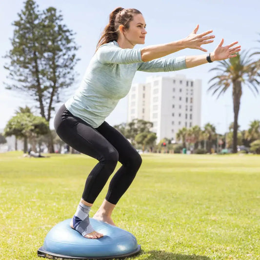 Open-heel ankle support in gray knit with navy straps worn during balance exercise
