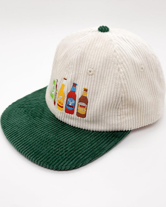 Cream cap with green brim, side view showing beer bottle patches and small top knot