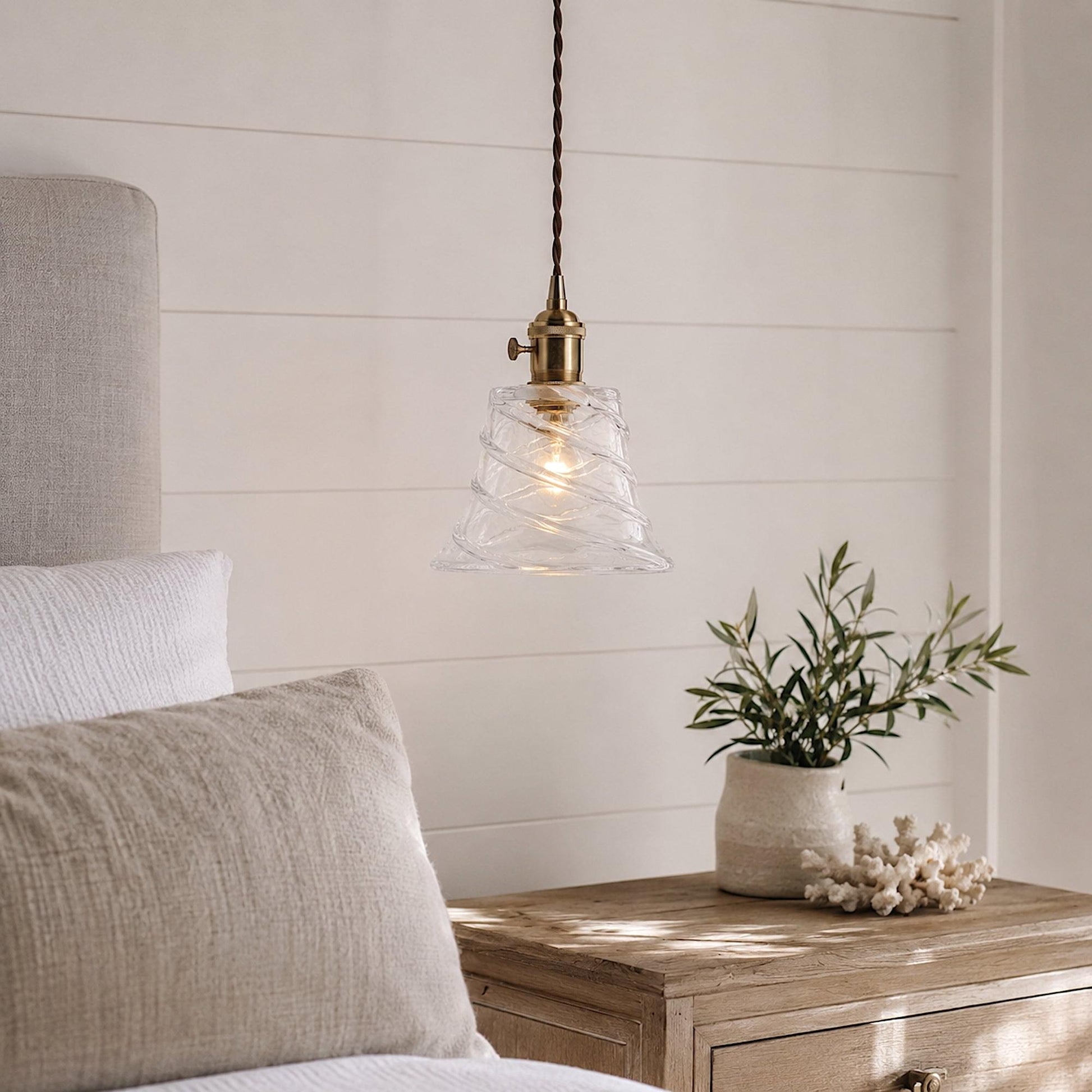 Clear glass pendant light with brass-toned socket and warm glowing bulb