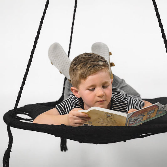 Black macrame hanging hammock swing with child reading in seat