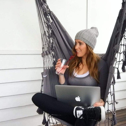 Charcoal hammock chair with fringed ropes and net seat, woman holding drink