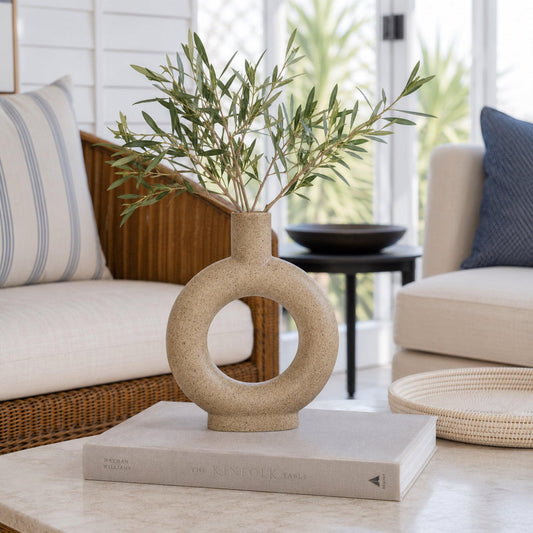 Beige ceramic vase with circular cutout ring and tall neck, holding greenery