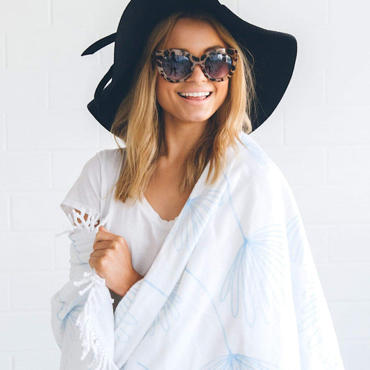 Round beach blanket/towel draped over shoulders, white with light-blue dandelion print