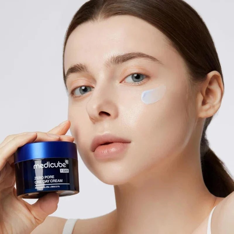 Woman applying blue-lidded cream jar; white cream dots on face for skincare