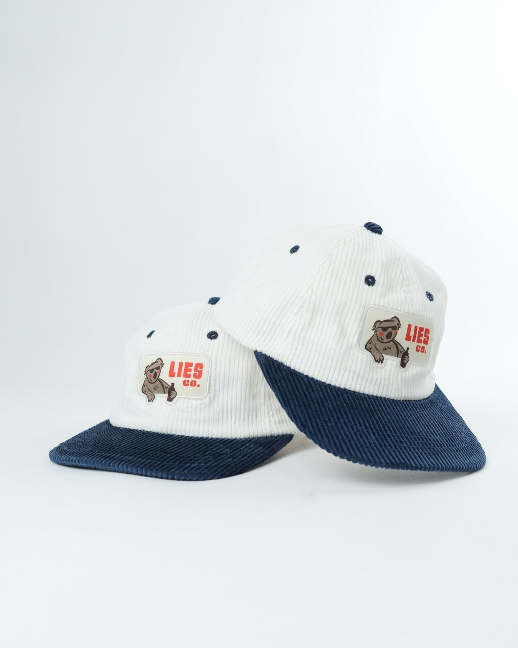 Two white knit koala graphic caps with navy brims and LIES CO. logo patches
