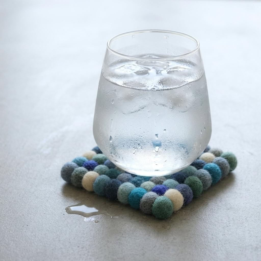 Round wool felt coaster with multicolor pom-pom border under a glass
