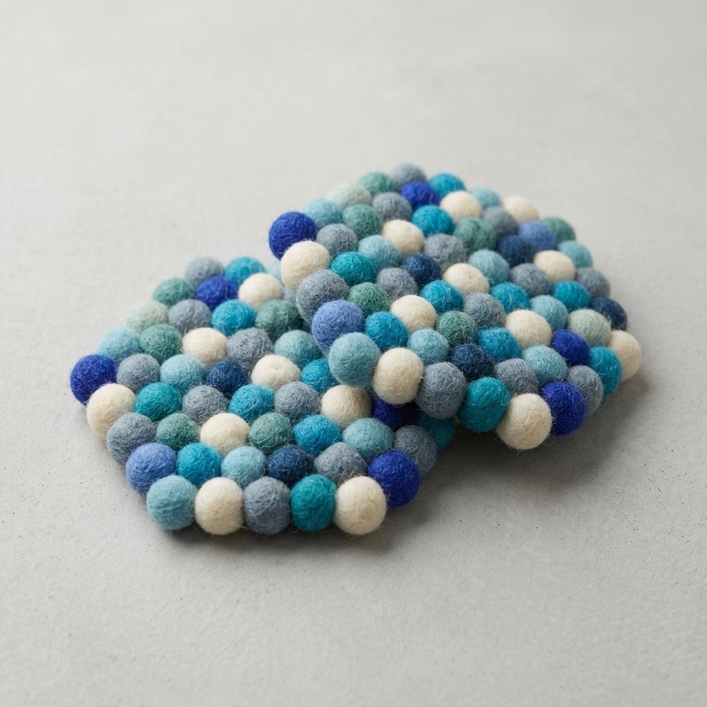 Round wool felt coaster with colorful pom-pom top in layered blues, greens, and cream