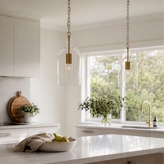 Clear glass pendant lights with gold chains and warm bulbs over kitchen island