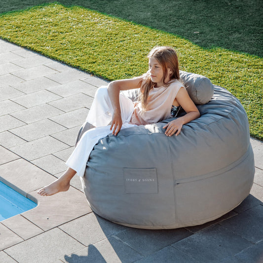 Grey bean bag chair outdoors with large cushioning and side storage pocket