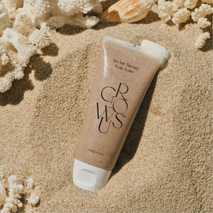 Sea salt scalp scrub tube on sandy beach with scattered white salt granules