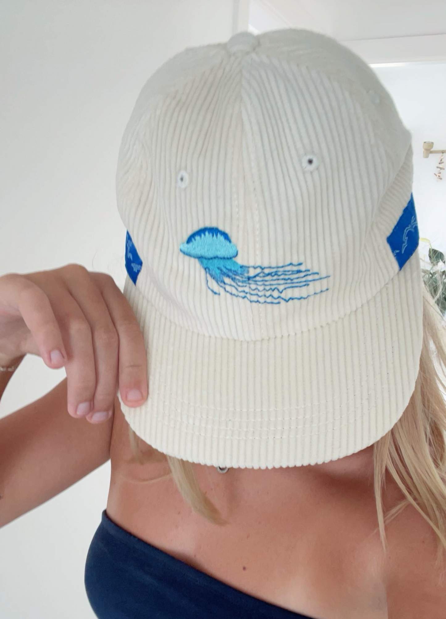 White ribbed bucket-style cap with blue jellyfish-and-waves embroidery and small eyelets.