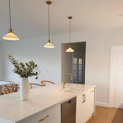 Multiple ceramic pleated pendant lights with white shades hanging from brass ceiling hooks