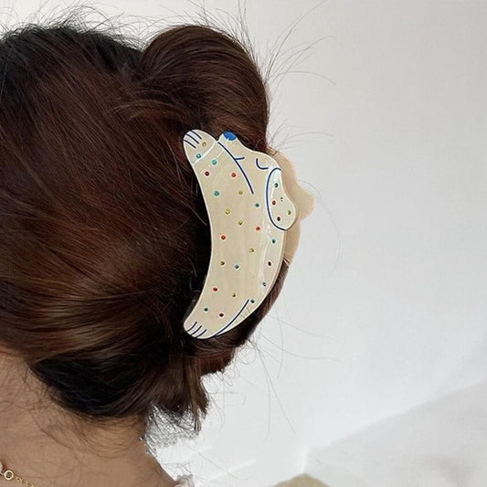 White puppy hair claw clip with colorful rhinestones, worn in brown hair.