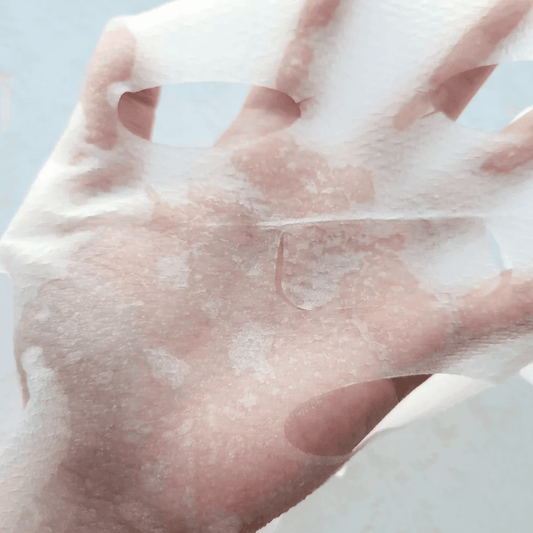Face mask sheet held in hand, thin translucent white sheet with visible serum