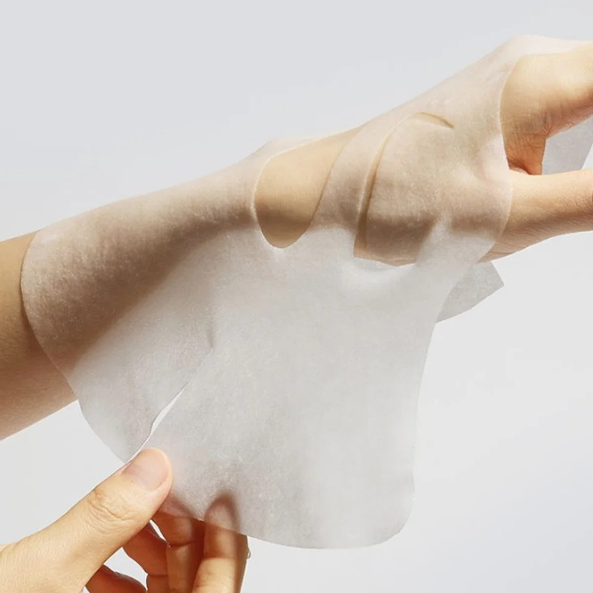 Slim translucent face mask sheet held up, showing eye and mouth cutouts