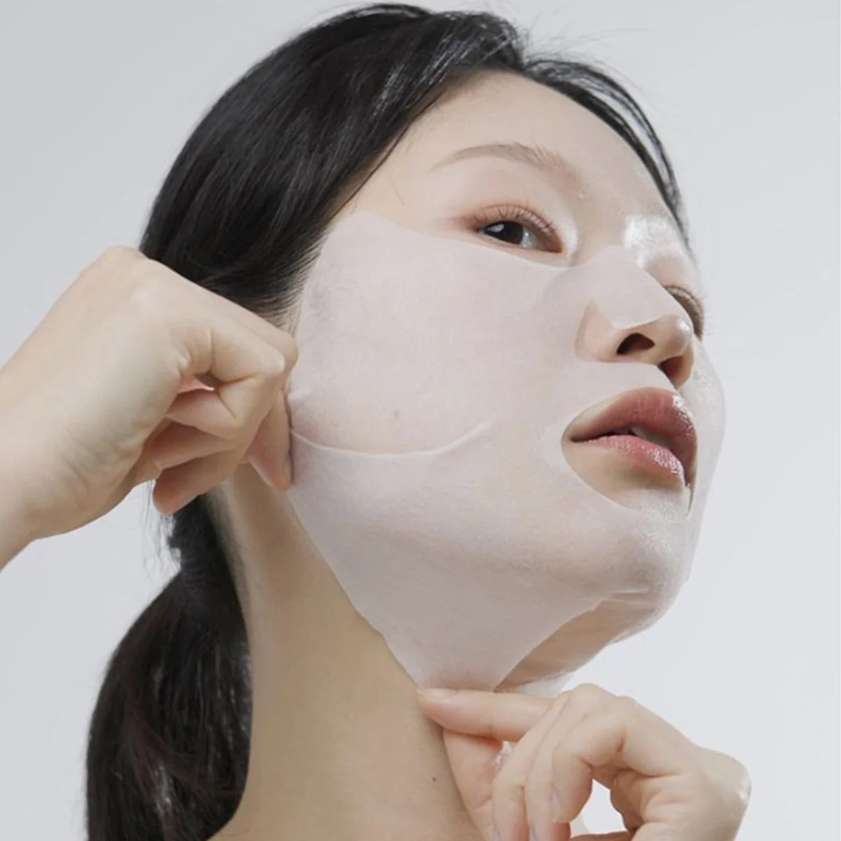 Translucent facial sheet mask covering nose and cheeks, held by hands