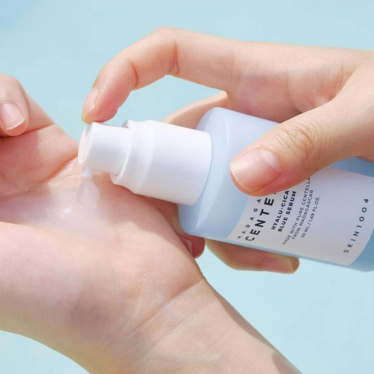 Hands holding a light blue serum bottle with white pump dispensing into palm.