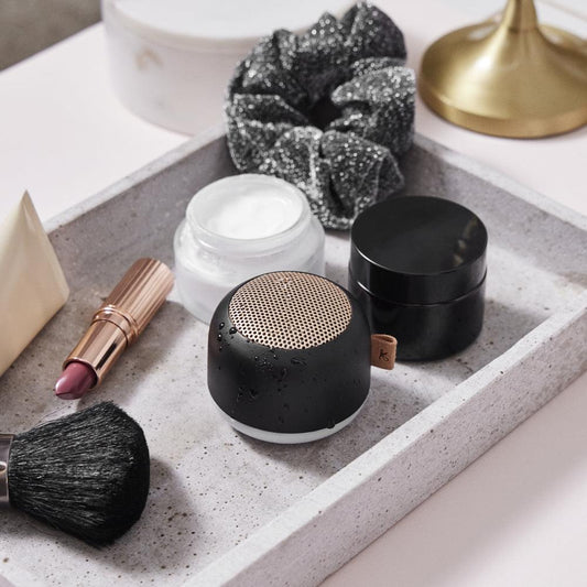 Black Bluetooth speaker on tabletop with metal grille speaker top