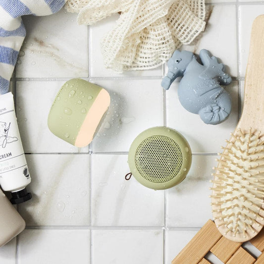 Olive portable Bluetooth speaker with black mesh grille on white tiled surface