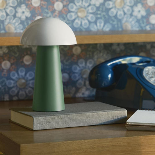 Portable table lamp with white dome shade and green base on gray book