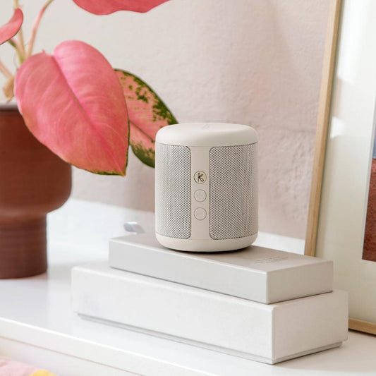 Soft white Bluetooth speaker on table, with top grille and side control buttons