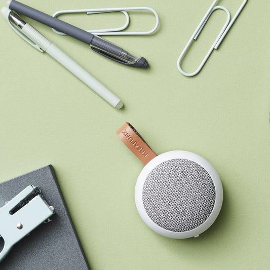 White Bluetooth speaker with gray fabric grille and brown leather strap, top view
