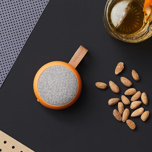 Dusty orange fabric Bluetooth speaker with gray grille, wrist strap loop visible