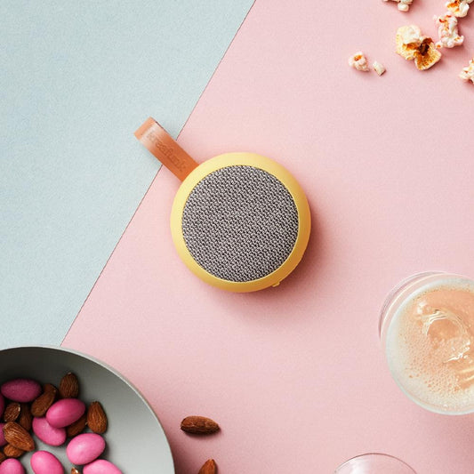 Soft yellow Bluetooth fabric speaker with gray round grille, near-top view