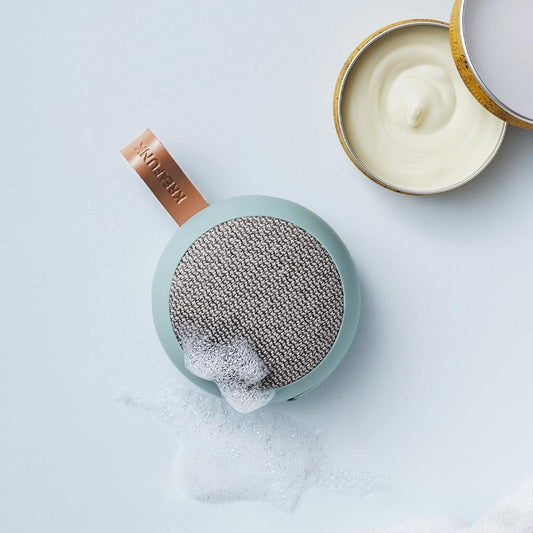 Dusty green fabric Bluetooth speaker with textured grille and leather tag