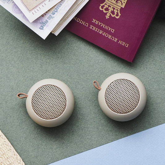 Pair of ivory mini Bluetooth speakers with circular grille faces and wrist straps