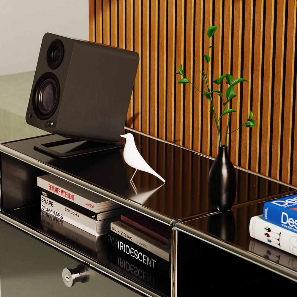 Matte black powered speaker tilted on shelf, showing woofer and tweeter